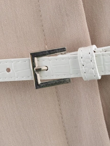 Detail of a white crocodile pattern belt with a square silver metal buckle on khaki fabric