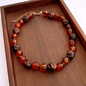 Détail du collier de perles en acrylique marron mat et ambre sur plateau en bois foncé