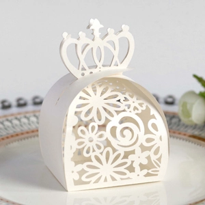 Macro shot of white laser-cut wedding favor box with crown handle on porcelain plate