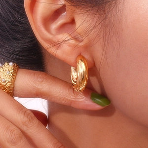 Close-up of 18K gold-plated C-shaped twisted croissant hoop earrings on a model's ear