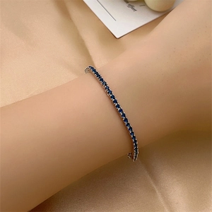 Detail of silver tennis bracelet with blue round zircons on champagne satin background