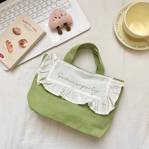 Detail showing avocado green canvas tote with white ruffle trim and Summerparty embroidery