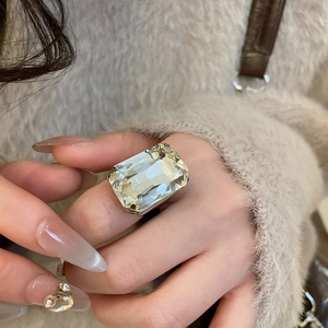 Macro shot of a large square-cut rhinestone ring on finger with elegant beige sweater