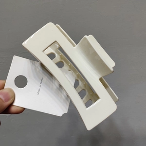 Close-up of a cream-colored hollow square hair claw clip held against a grey wall