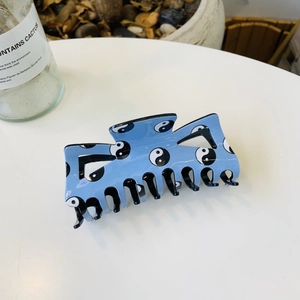 Blue acrylic hair claw clip with Tai Chi Yin Yang design on a white surface