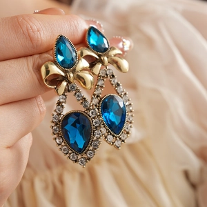 Close-up of vintage gold earrings featuring teardrop blue gemstones and crystal accents