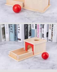 Detail of wooden Montessori object permanence box with red ball and storage drawer