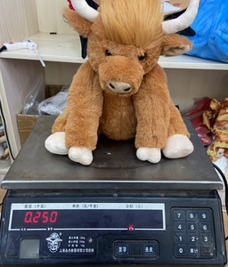 Detailansicht der Gewichtsangabe eines braunen Highland Cow Plüschtiers auf einer Waage