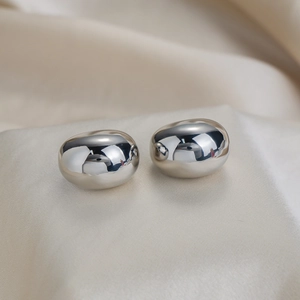 Macro view of polished mirror finish pebble earrings on soft satin fabric texture