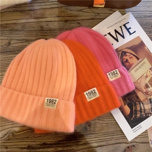 Close-up of pink and orange knitted beanies with California 1982 tags on wood background