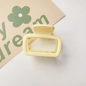 Detail of a square yellow plastic hair claw clip with internal teeth on a white card