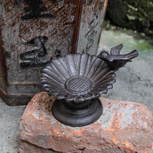 Rustic cast iron sunflower bird feeder with small bird figurine on red brick base