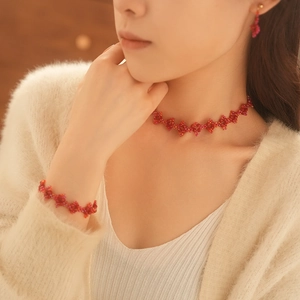 Detail of red beaded jewelry set with rhombus patterns on a model wearing beige sweater