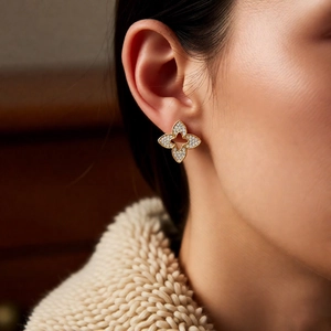 Close-up of gold-plated clover earrings with white zircon pavé on model's ear