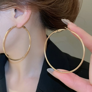 Close-up of large polished gold hoop earrings worn on ear with high-gloss mirror finish