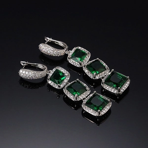 Macro shot of silver tiered long drop earrings with square green crystals on black mirror