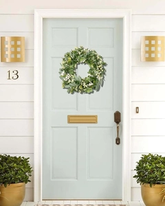 Close-up of artificial eucalyptus wreath with white berries hanging on a light blue door