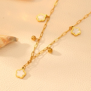 Macro shot of gold stainless steel necklace with white four-leaf clover and beads