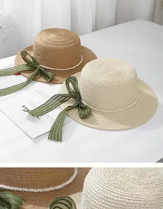 Flat top straw sun hats featuring pearl bands and dark green ribbon bows on a table