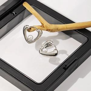 Détail de boucles d'oreilles cœur en perles argentées dans un écrin de luxe
