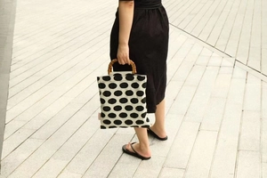 Detail of vintage polka dot canvas tote bag featuring natural bamboo handles in street setting