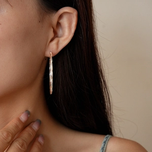 Close-up of a model wearing large silver-polished twisted geometric hoop earrings for women