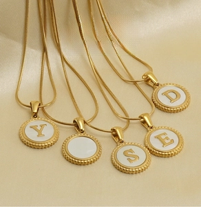 Macro detail of 18K gold snake chain necklaces with shell inlaid alphabet pendants