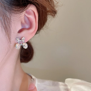 Detailed close-up of sparkling silver bow earrings set with clear oval crystals on model