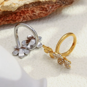 Détail de bagues fleurs or et argent serties de zircons sur une surface texturée