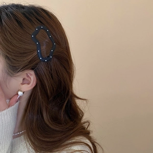 Detail of a black polka dot hair clip styled on wavy hair with pearl accessories