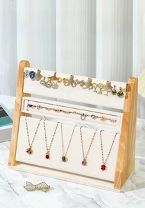 Three-tier wooden jewelry display stand with beige velvet panels on marble surface