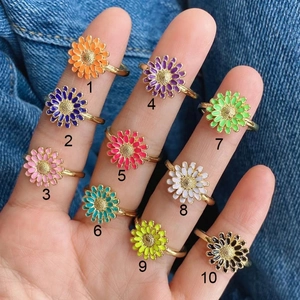 Detail of 10 colorful enamel daisy rings with copper bands shown on denim background