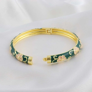 Detail of green enamel hinge bracelet with pink floral patterns on a white silk background