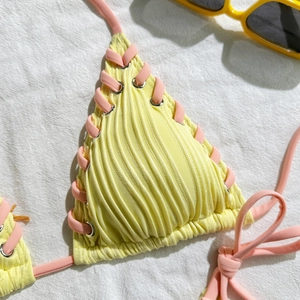Detail of yellow ribbed bikini fabric with pink side-ties and silver eyelets