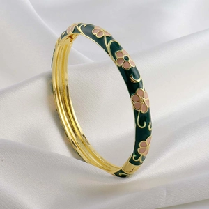 Detail view of green enamel cuff bracelet with pink floral motifs on white silk fabric