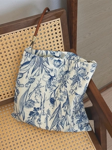 Vintage blue floral canvas bag with brown leather handles on a woven rattan chair