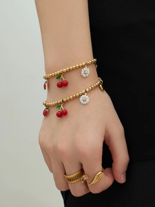 Détail d'un bracelet plaqué or 18k avec breloques cerise et marguerite sur un mannequin