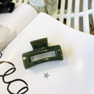 Detail of a square dark green hair claw clip with a glossy finish on a white book
