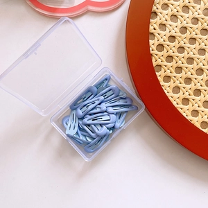 Detail showing multiple light blue candy-colored metal hair clips in a clear plastic box