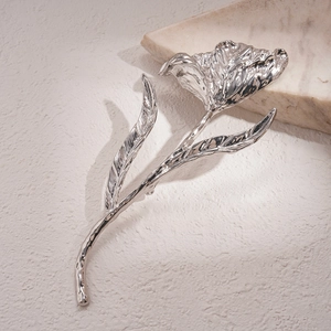 Detailed close-up of a silver tulip brooch with a polished mirror finish on textured fabric