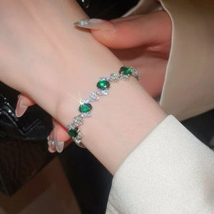 Detailed view of silver oval green zircon bracelet on model wrist with leather backdrop