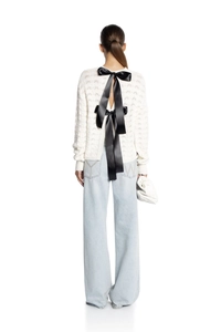 Detail of white hollow knit top featuring dual black satin back bows with blue denim jeans