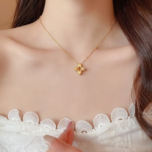 Close-up of golden four-leaf clover pendant necklace with zircon on female model