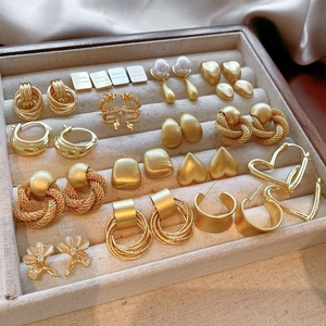 Macro shot of assorted gold earrings with geometric and heart shapes on a velvet tray