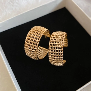 Close-up of golden mesh C-shaped hoop earrings with a textured woven surface design