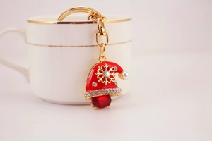 Detail of a red enamel Santa hat keychain with crystals and pearls on a white cup