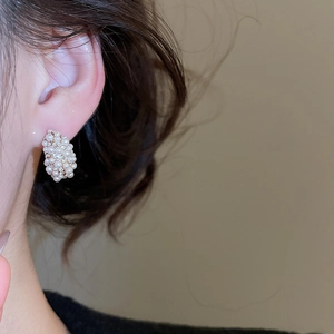 Close-up of elegant C-shaped earrings with pearls and zircons worn on model ear