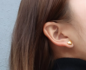 Close-up of golden heart earrings worn by a model to show size and high-shine finish