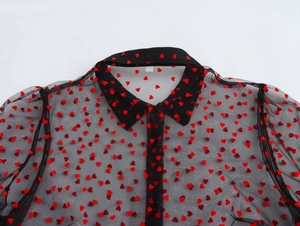 Detail of sheer black mesh shirt featuring red flocked hearts and ruffled lantern sleeves