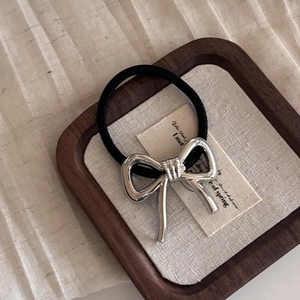 Minimalist silver metal bow hair tie with black elastic band on a wooden tray